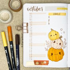 an open planner with pumpkins on it next to markers and pens