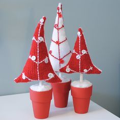 three knitted christmas trees sitting on top of red cups with white snow in them