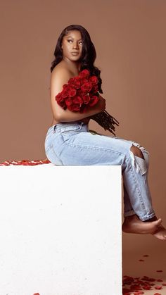 a woman sitting on top of a white box with red flowers in her hair and jeans