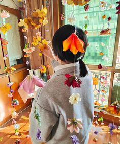 a woman standing in front of a window with paper flowers on her head and an umbrella hanging from the ceiling