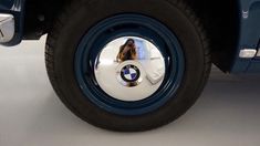 the front wheel of a blue car with a woman's reflection in it