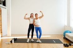 two women standing on a yoga mat with their arms in the air and one holding her fist up