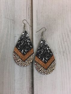 a pair of black and brown glittered tear earrings on top of a wooden table