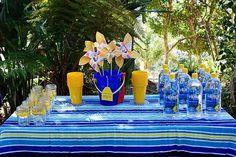 a blue table cloth with yellow vases and water bottles on it in front of trees