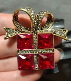 a person is holding a red and gold bow brooch with diamonds on the sides