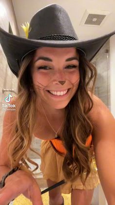 a woman wearing a cowboy hat and holding a knife in front of her face while smiling at the camera