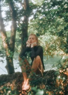 a woman sitting on top of a tree next to a body of water with trees around her