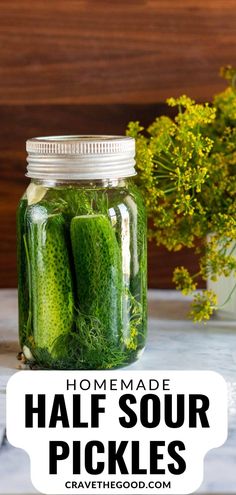 homemade half sour pickles in a mason jar with flowers behind it and text overlay that reads homemade half sour pickles