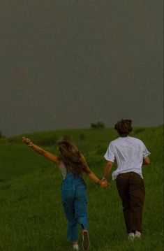 two people holding hands while flying a kite in a field with dark clouds above them