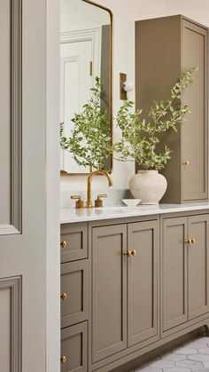 a bathroom with gray cabinets and gold accents on the mirror above it is a plant in a white vase