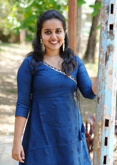 a woman in a blue dress standing next to a wooden pole smiling at the camera