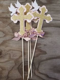 two pink and gold cupcake toppers with angel wings on them, one has a cross