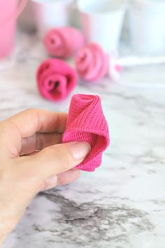 a person is holding a pink knitted object on a marble table with other items in the background