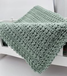 a green crocheted blanket sitting on top of a white shelf