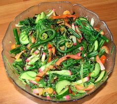 a glass bowl filled with lots of veggies on top of a wooden table