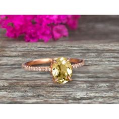 a yellow diamond ring sitting on top of a wooden table next to pink flower petals