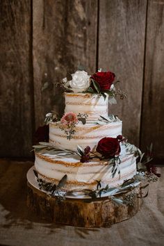 a three tiered wedding cake with flowers and greenery sits on a wooden table