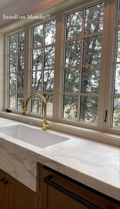 a kitchen with marble counter tops and wooden cabinets in front of large windows that look out onto the woods