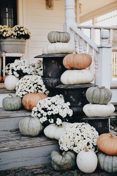 white and orange pumpkins are stacked on the porch steps with daisies in vases