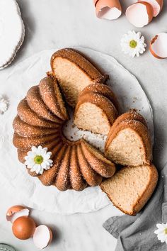 a bundt cake with slices cut out on a plate next to eggs and flowers