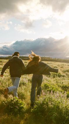 two people are running through the grass with their arms around each other