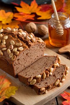 sliced loaf of bread with nuts and honey on wooden cutting board next to autumn leaves