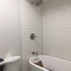 a white bath tub sitting under a faucet next to a toilet paper dispenser