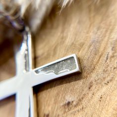 a silver cross on a wooden table with a feather hanging from it's end