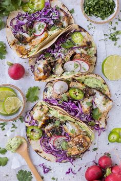 three fish tacos with cabbage, avocado and cilantro on the side