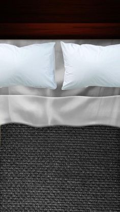 a bed with two white pillows and black carpet