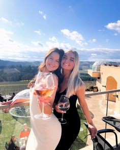 two beautiful women standing next to each other holding wine glasses