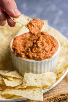 a hand dipping some tortilla chips into a bowl