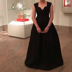 a woman in a black dress standing next to a glass case with jewelry on it