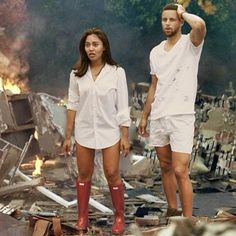 a man and woman standing next to each other in front of a destroyed building with fire coming from the roof