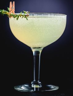 a glass filled with a liquid and garnished with herbs on the rim, sitting on a black surface