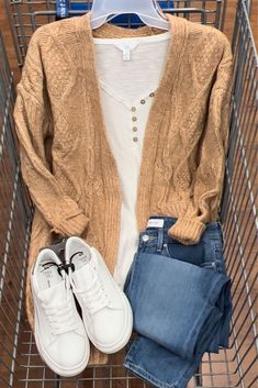 a pair of white shoes sitting on top of a shopping cart next to a sweater and jeans