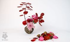 a vase filled with red and pink flowers on top of a white table next to dried leaves