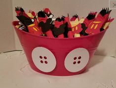 a pink bowl filled with lots of paper cut out of mickey mouse ears and faces