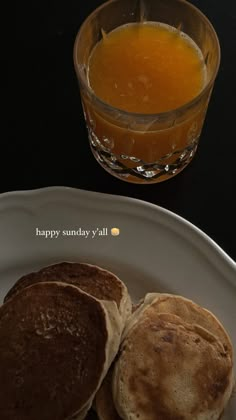 two pancakes on a white plate next to a glass of orange juice and a black table