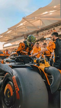 several men in orange and black racing gear sitting on top of two large gray tires