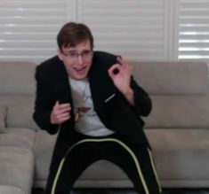 a man sitting on top of a couch in front of a white wall holding a remote