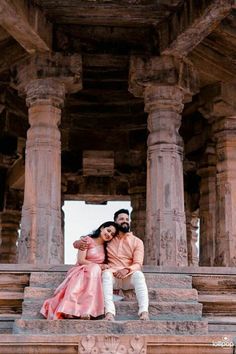 a man and woman sitting on the steps of an old building with pillars in front of them