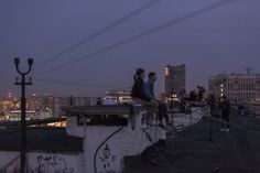 people are sitting on the roof of a building at night with city lights in the background