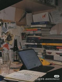 a laptop computer sitting on top of a desk next to a pile of books and papers