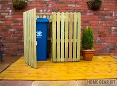 a wooden fence with a blue trash can next to it and potted plants on the side