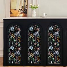 a black cabinet with flowers painted on the front and sides, next to a vase filled with flowers