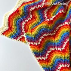 a crocheted blanket is laying on top of a white surface with an orange, yellow, red, and blue pattern