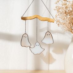 two white ghost ornaments hanging from chains next to a vase with dried flowers in it