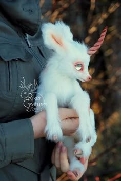 a person holding a small white animal in their hands and it looks like a unicorn