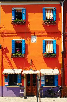 an orange building with blue shutters and two bicycles parked in front of the windows